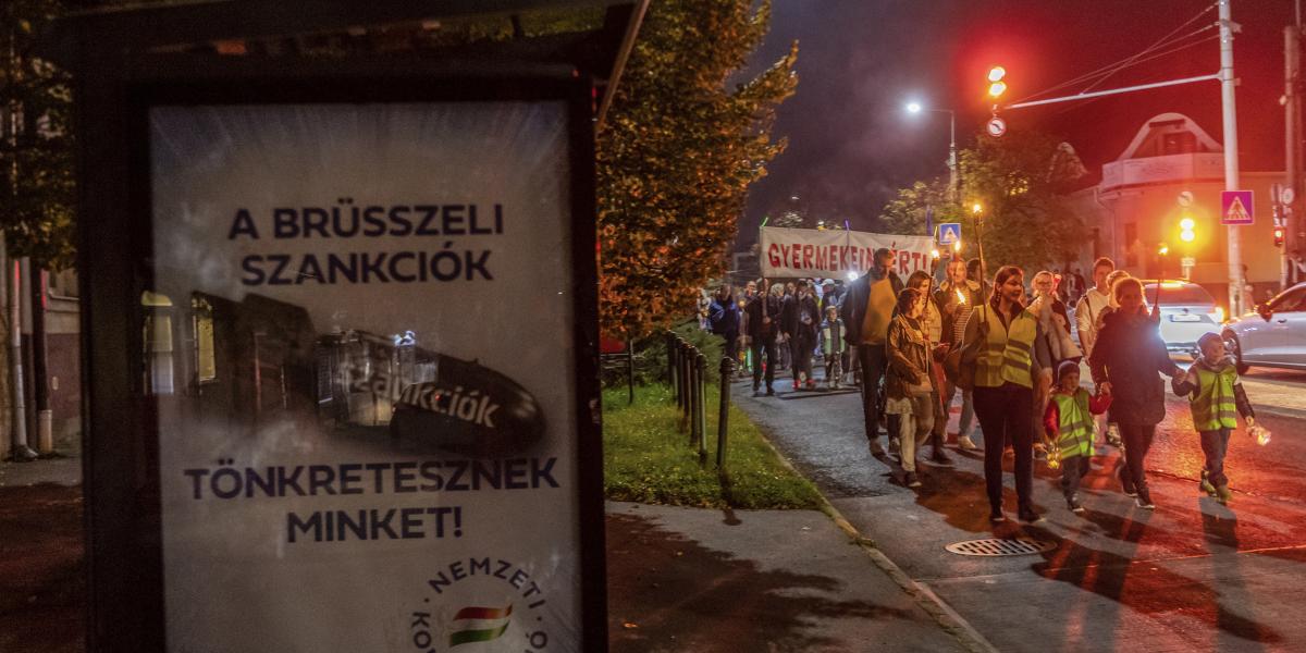 Kormányzati propagandaplakát előtt vonulnak a tanártüntetés résztvevői Budaörsön. A településeknek most azt a kormányzatot kellett volna segíteniük szignójukkal, amelyik nem ad elég pénzt tanáraik, iskoláik számára