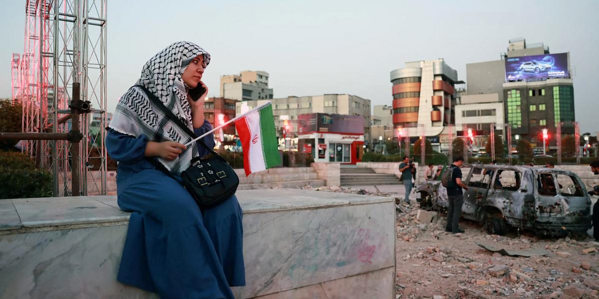 Egy iráni nő egy felrobbantott jármű közelében ül a Hafteh-tir téren, Teheránban, 2025. június 23-án