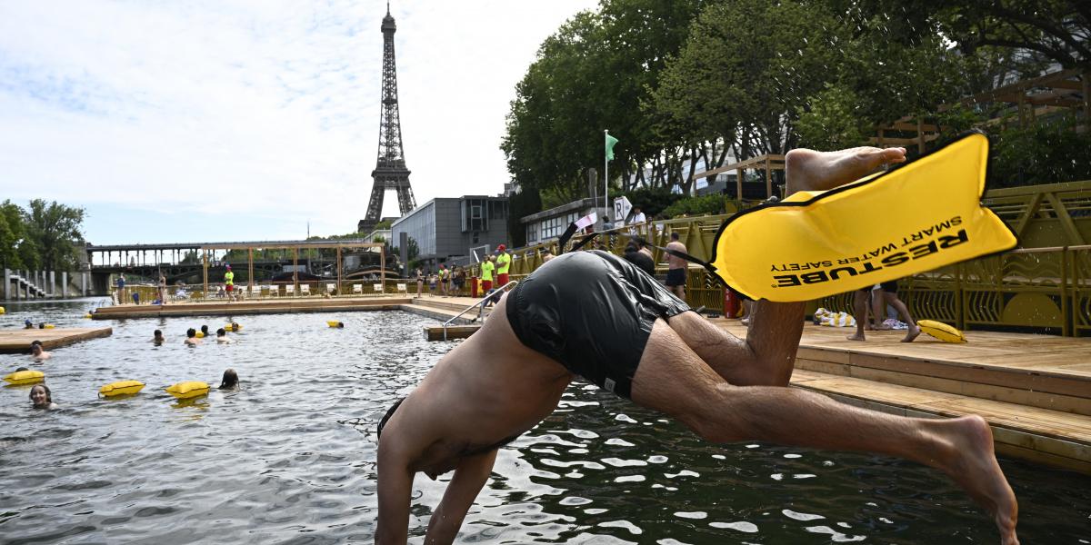 Egy úszó mártózik a vízben a Szajna folyón található Grenelle fürdőhelyen a megnyitó napján, az Eiffel-torony előtt Párizsban, 2025. július 5-én
