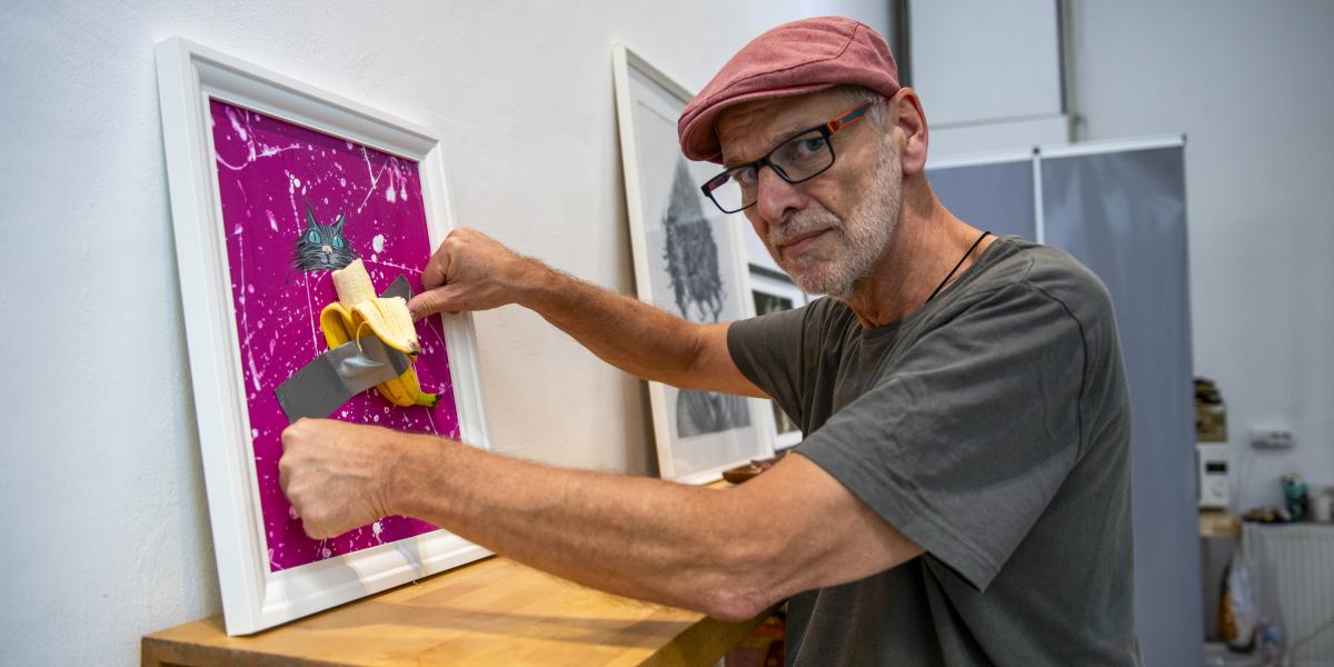 Pápai Gábor karikaturista a szombati kiállításmegnyitó előtt banánt fog ragasztani a művére