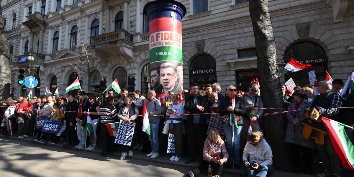 Illusztráció: Tisza-szimpatizánsok várakoznak egy Fidesz-plakát mellett március 15-én 