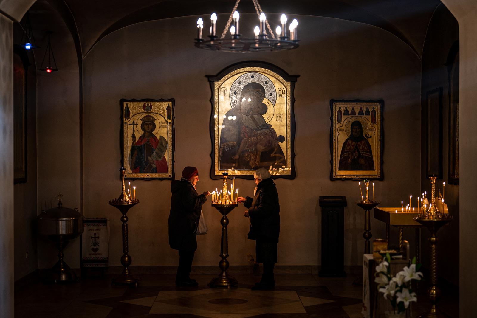 Egy nő a kórusban nagyítót használ egy ortodox húsvéti istentisztelet alatt, a távolban folyamatos ágyúzás hangjai hallatszanak a kelet-ukrajnai Lymanban lévő Szent Péter és Pál templomban 2022. április 24-én, az ukrajnai orosz invázió közepette.