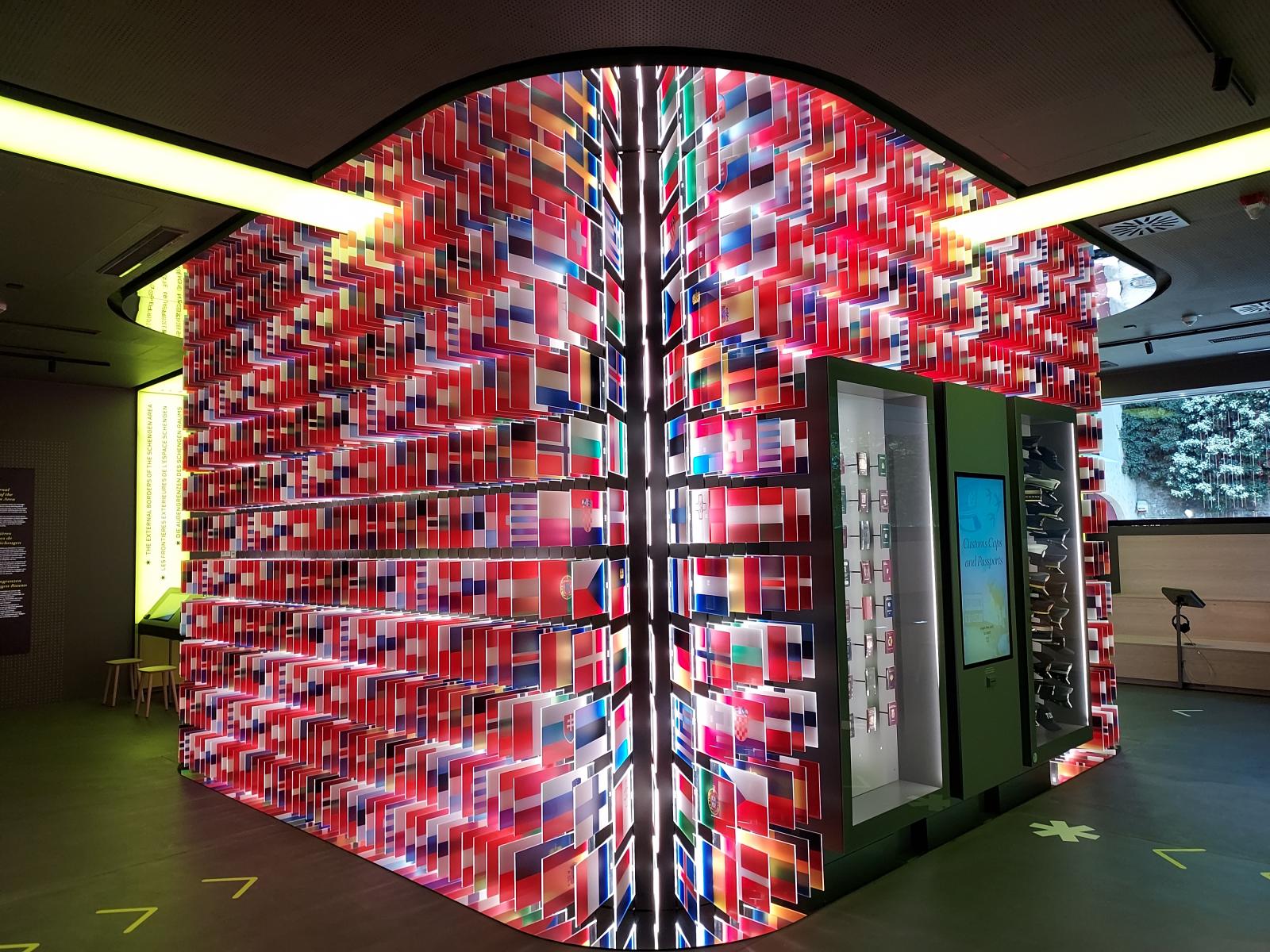 A Schengeni terület 29 országának zászló kavalkádja a múzeumban; rajta és körülötte interaktív ismerkedés Schengen mibenlétével, ahol semmihez sem tilos hozzáérni – sőt!