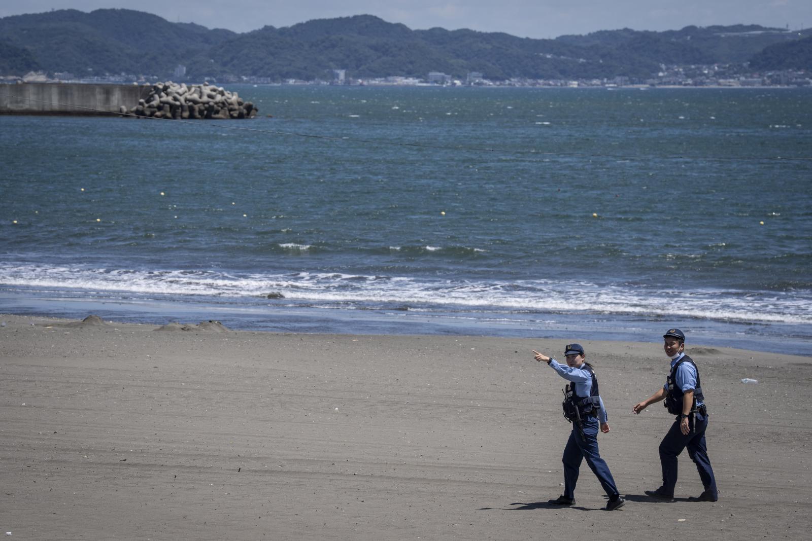 Rendőrök figyelmeztetik a lakosokat, hogy a cunamiriadó miatt hagyják el a strandot Japánban, Fujisawa városában