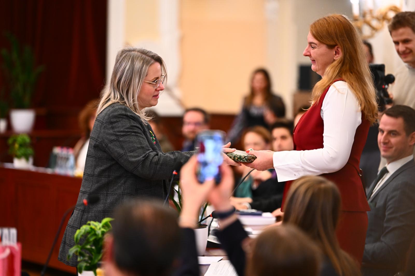 Szepesfalvy Anna adja át Baranyi Krisztina ajándékát, a Fővárosi Közgyűlésen, december 17-én