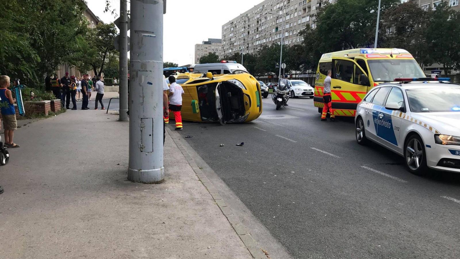 Mentősök, rendőrök a Szentendrei úton felborult taxi körül