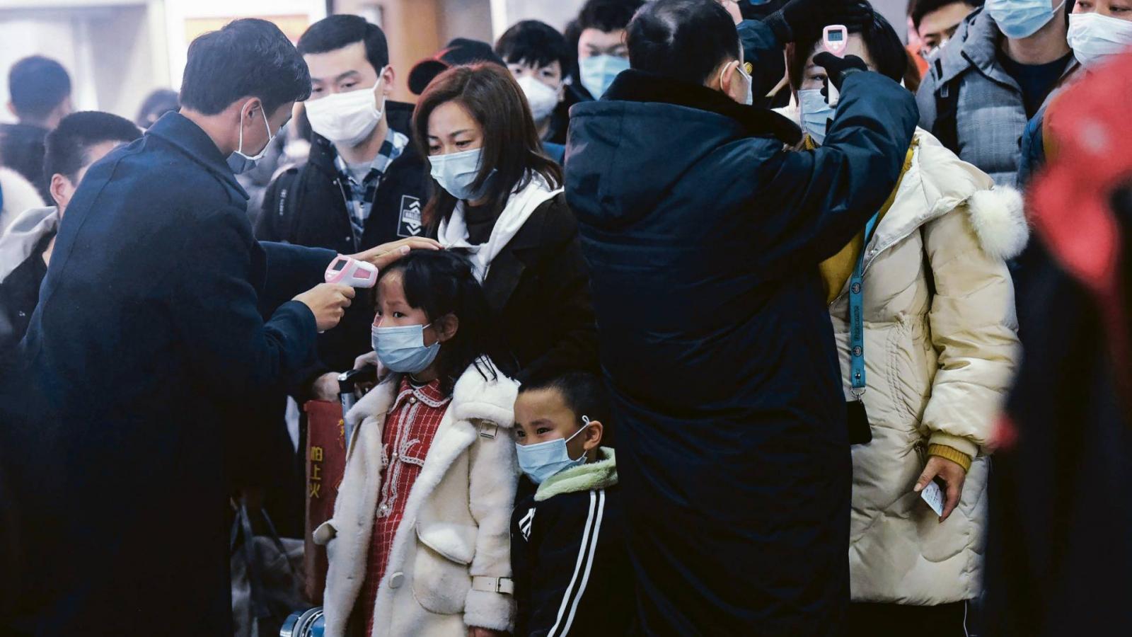 Fekete ruhás egészségügyi alkalmazottak mérnek testhőmérsékletetet a Hangzhou Vasútállomáson, ahova egy vonat futott be Vuhan városából