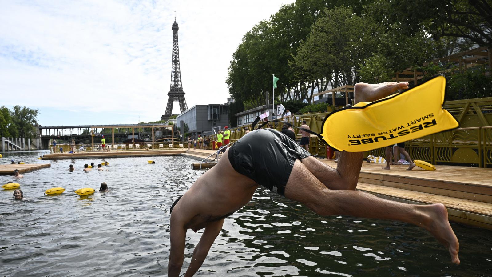 Egy úszó mártózik a vízben a Szajna folyón található Grenelle fürdőhelyen a megnyitó napján, az Eiffel-torony előtt Párizsban, 2025. július 5-én