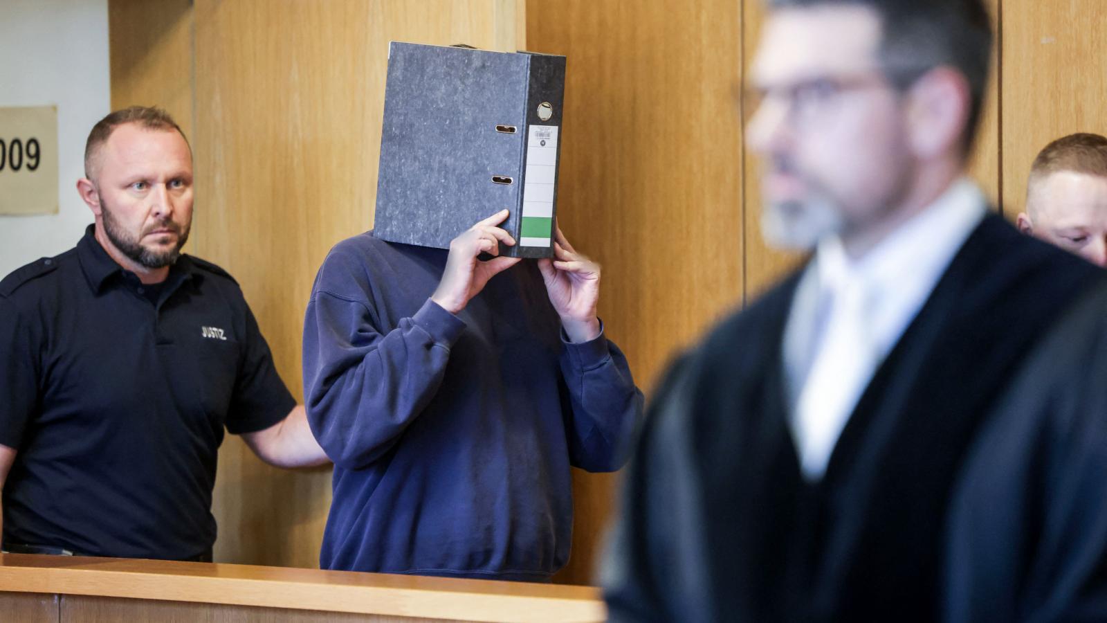 A vádlott ápoló egy irattartóval az arca előtt a tárgyalóteremben.